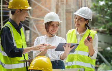 Architects wearing safety helmet discussing, planing, measuring layout at construction site.	