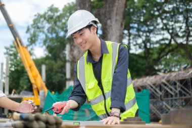 Smart civil engineer manager wearing safety helmet and vast  inspecting and working at structure building site with blueprints.