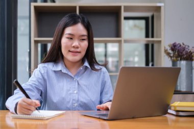 Smiling young female employee using laptop on wooden office desk.	
