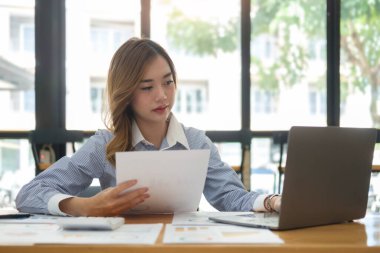 Beautiful asian businesswoman using laptop computer and checking financial document at office desk.	