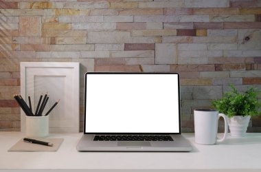 Laptop, coffee cup, potted plant, picture frame and supplies on white table. Blank screen for your advertise.