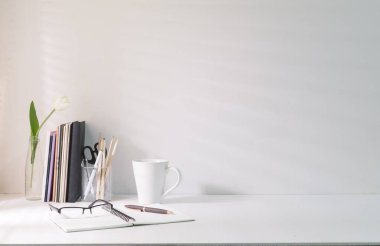 Minimal workplace with coffee cup pencil holder notebook and flower pot on white table. Copy space for your advertise text.