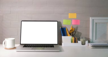 Stylish workplace with laptop, coffee cup, houseplants and stationery on white table.	