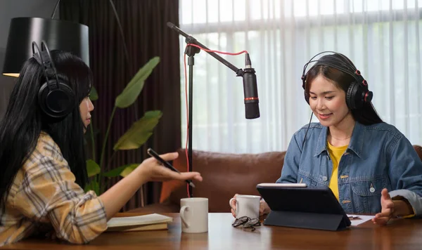 Two young women radio hosts using microphone and audio mixer recording podcast at home studio togrther.