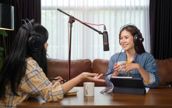 Female radio host interviewing guest while broadcasting live audio podcast in home studio at night.