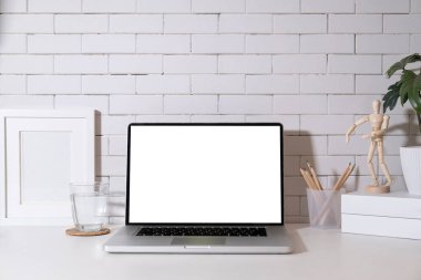 Laptop, saksı, kahve fincanı, resim çerçevesi ve beyaz masanın üzerinde bir bardak su. Reklam metniniz için boş ekran.