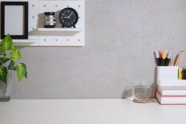 Kitapları, camları, kırtasiyesi ve beyaz masasında çiçekleri olan yaratıcı, şık bir iş yeri. Merkez ofis masası.