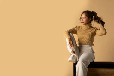 Bej arka planda oturan, modaya uygun sonbahar kıyafetleriyle poz veren çekici bir kadının panoramik çekimi. Reklam metniniz için alanı kopyalayın.