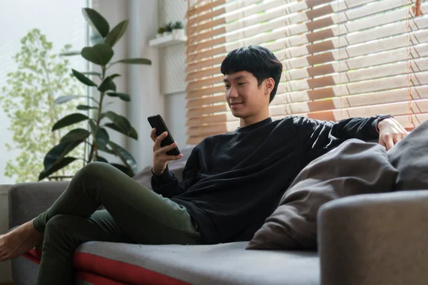 Young Asian Man Resting Sofa Using Smart Phone — Stock Photo, Image