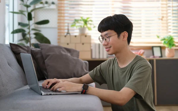 微笑英俊的亚裔男子坐在客厅的地板上 用笔记本电脑 — 图库照片