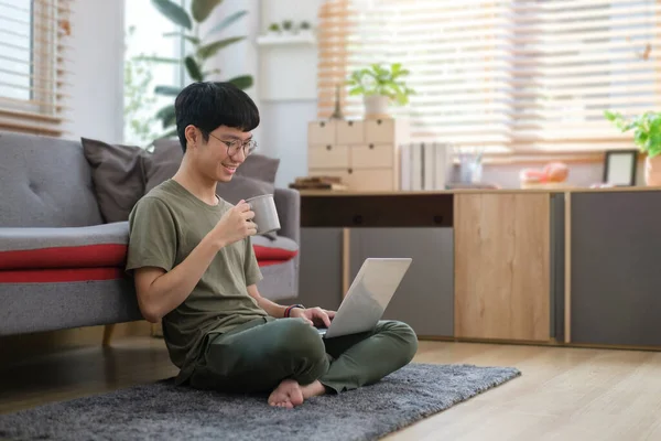 穿着休闲装的快乐男人坐在舒适的家的地毯上 用笔记本电脑上网 — 图库照片
