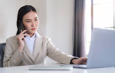 İş kadını ofiste otururken cep telefonuyla konuşuyor.