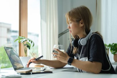 Bir bardak su tutan ve dizüstü bilgisayarla çalışan serbest çalışan kadın..