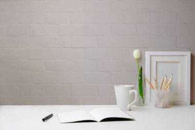 Resim çerçeveli ofis masası, kahve fincanı, lale ve not defteri beyaz masada. Metnin için boşluk kopyala.
