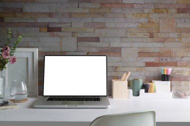 Home office desk with laptop, coffee cup, picture frame and stationery on white table.	