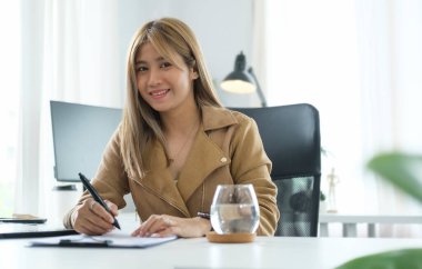 Bin yıllık kendine güvenen bayan girişimci kişisel ofisinde oturuyor ve kameraya gülümsüyor..