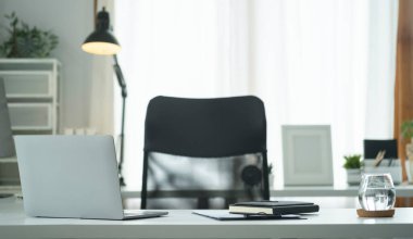 Laptop bilgisayar, bir bardak su, ve modern ofisteki beyaz masada malzemeler..