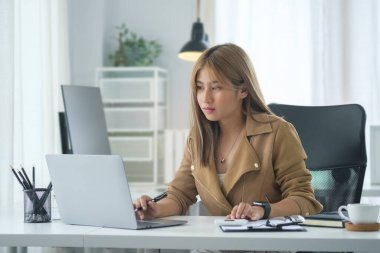 Modern iş yerinde dizüstü bilgisayarla çalışan genç yaratıcı kadın..