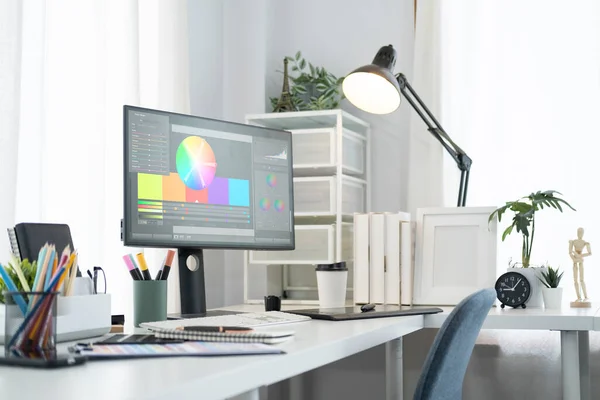Yaratıcı bir iç mekan. Spektrum renk tekerli bilgisayar monitörü, beyaz masada malzeme ve lamba. 