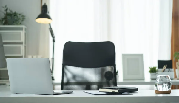 Laptop bilgisayar, bir bardak su, ve modern ofisteki beyaz masada malzemeler..