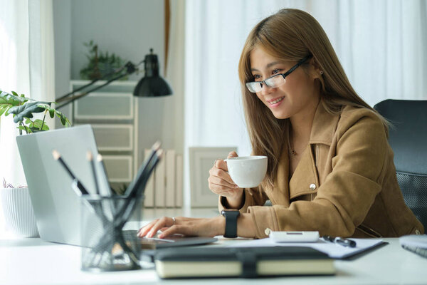 Happy young businesswoman drinking coffee and working at bright office.
