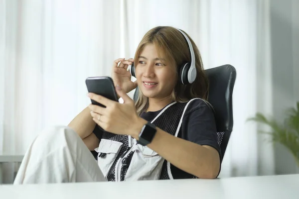 Pleased young woman with wireless headphone using mobile phone in home office.