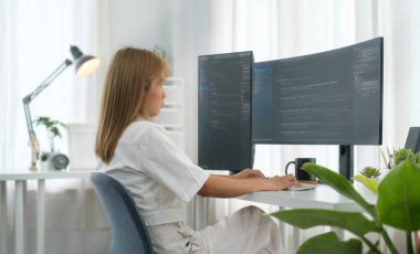 Yazılım geliştiricisi serbest çalışan kadın modern ofiste geniş ekranlarda program kodu ile çalışıyor..