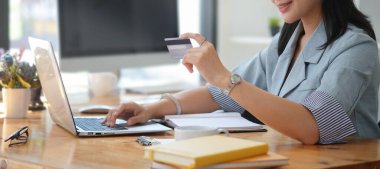 Elinde kredi kartı olan gülümseyen genç bir kadın online bankacılık işlemleri ve e-ticaret için laptop kullanıyor..