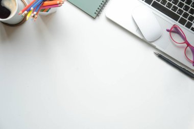 Düz dizüstü bilgisayar, gözlük, kahve fincanı ve kırtasiye malzemesi beyaz masada duruyordu. Metnin için boşluk kopyala.