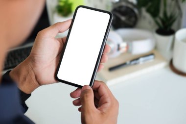Close up view businessman holding smart phone with blank screen while standing in modern office.