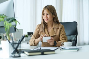 Genç iş kadını bilgisayar ekranına bakıyor ve ofis masasında hesap makinesi kullanıyor..