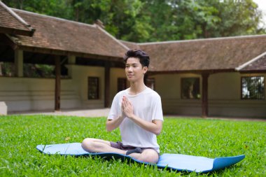 Yeşil çimlerin üzerinde lotus pozisyonunda meditasyon yapan bir adam. Yoga, pilates, spor, sağlıklı yaşam tarzı konsepti.