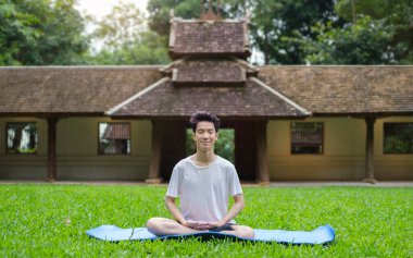 Barışçıl Asyalı adam yeşil çimlerde yoga meditasyonu yapıyor. Sakinlik ve meditasyon kavramı.