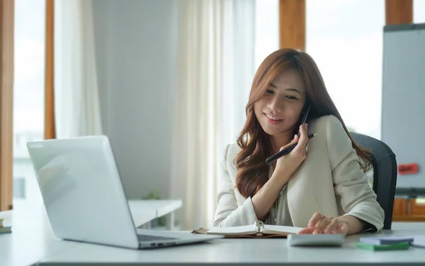 Cheerful Asian Female Employs Sitting Front Her Laptop Talking Mobile — Φωτογραφία Αρχείου