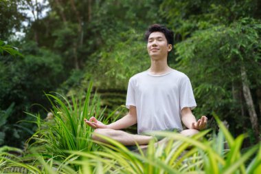 Yüzü gökyüzüne yükselmiş meditasyon yapan genç bir adam ve güzel doğayla çevrili açık havada gözleri kapalı bir adam..