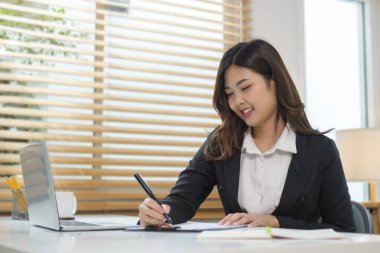 Parlak ev ofisinde oturan ve dizüstü bilgisayar kullanan hoş bir genç kadın..