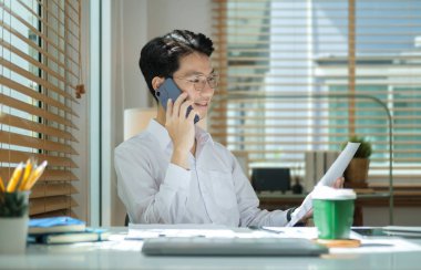 Genç bir iş adamı cep telefonuyla konuşuyor ve raporları kontrol ediyor..