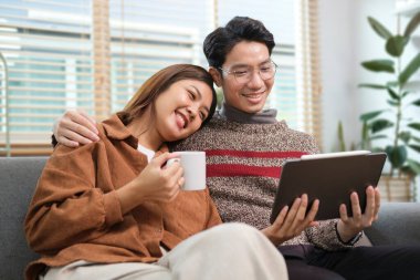 Kanepede dijital tablet kullanan neşeli genç çift kış tatillerinin tadını çıkarıyor..