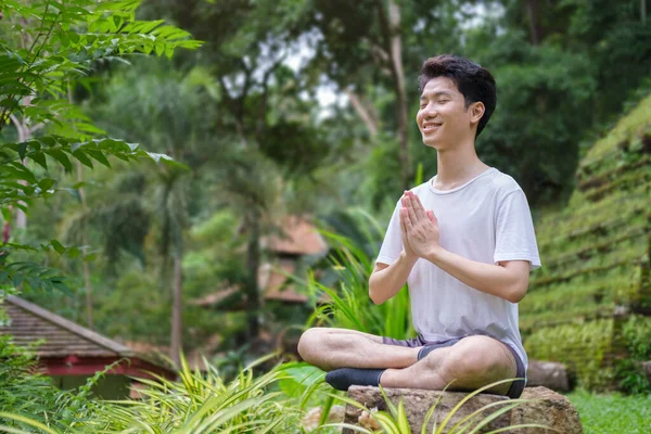 Man meditating and doing breathing exercise while sitting at outdoor surrounded by beautiful nature.