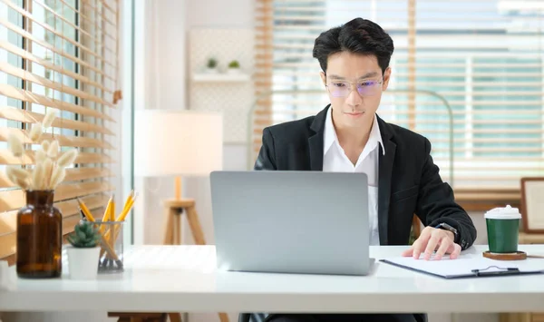 集中的男性财务顾问在办公室桌上使用笔记本电脑和编写合同文件 — 图库照片