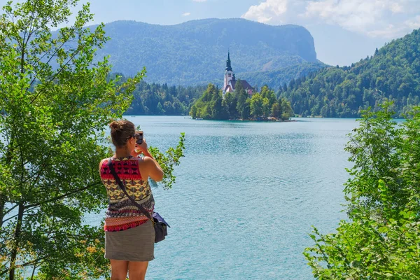 Lake Bled, Slovenia - August 20, 2018: A tourist girl takes a mobile photograph of Bled Island and its stunning surroundings