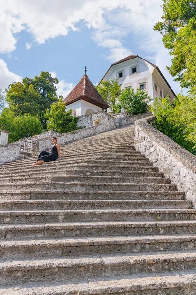 Lake Bled, Slovenia - August 20, 2018: A female tourist poses on the steps of Bled Island on a partly sunny summer day