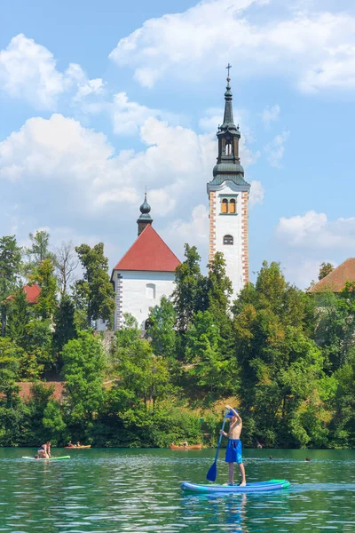 Lake Bled, Slovenia - August 20, 2018: Tourists enjoy the water in summer in front of the Assumption of Mary Church at Bled Island