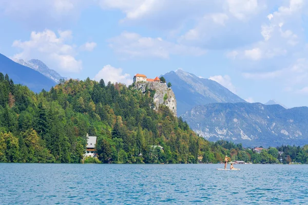 Lake Bled, Slovenia - August 20, 2018: People enjoy the water in summer while paddle-surfing in an alpine scenery with some magnificent architecture 