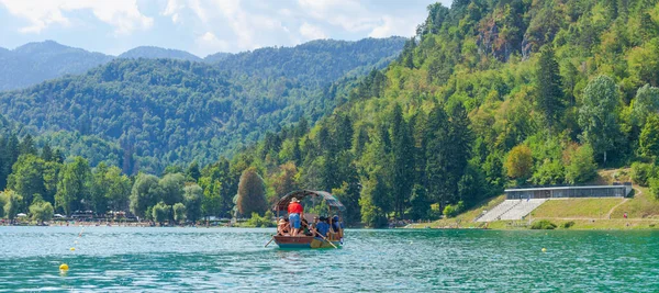 Lake Bled, Slovenia - August 20, 2018: Tourists enjoy a trip in a traditional 'pletna' wooden boat among an alpine landscape (pano)