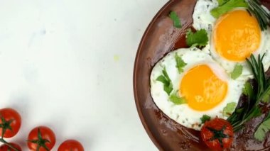 Seramik tabakta kızarmış yumurta, doğranmış maydanoz ve biberiye filizleri serpiştirilmiş, saat yönünün tersine döndürülmüş. Yakın plan..