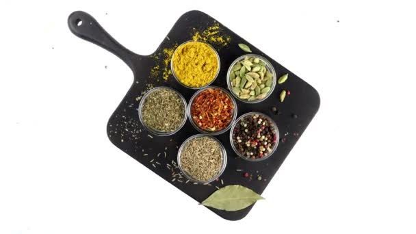 Olika indiska kryddor och örter roterade på vit bakgrund i glasskålar. Sortiment av färgglada asiatiska smakämnen, kryddor för matlagning mat. Ovanifrån. — Stockvideo