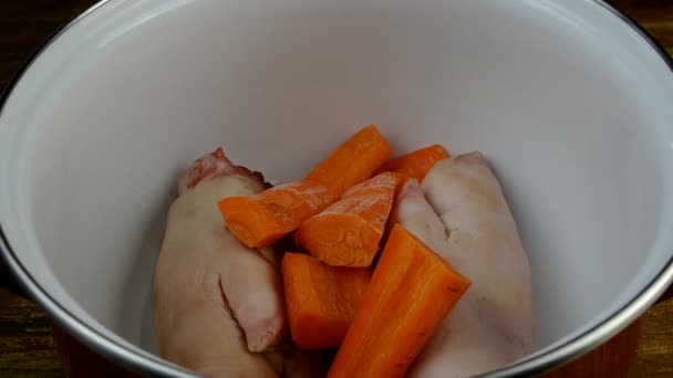 Rohe Schweinekeulen, Karotten, Zwiebeln, Selleriestängel, Lorbeerblatt, Pfefferkörner und Salz legen sich in einen Topf zur Zubereitung schmackhafter Brühe oder Aspik. — Stockvideo