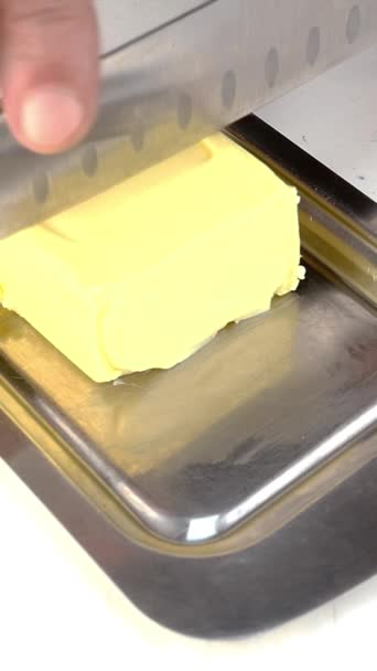 Hand schneidet Stück Butter mit großem Küchenmesser für die Zubereitung von Lebensmitteln. — Stockvideo