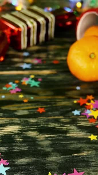 Hand legt Geschenkbox mit roter Schleife auf den Tisch, dekoriert mit weihnachtlichem Zeug, auf Bokeh-Girlanden-Licht. — Stockvideo